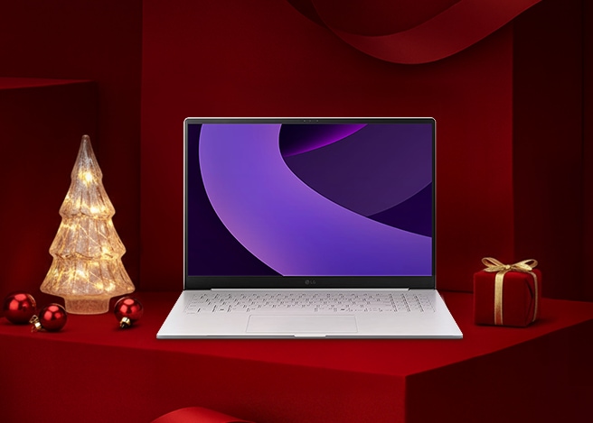 레드 기프트 박스 배경 위에 LG 그램 노트북이 놓여 있고, 좌측에는 조명 트리, 우측에는 리본이 묶인 선물이 배치된 연말 분위기의 구성.